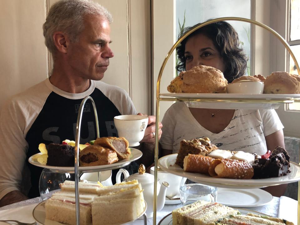 A man and a woman enjoying afternoon tea with trays of sandwiches and pastries.