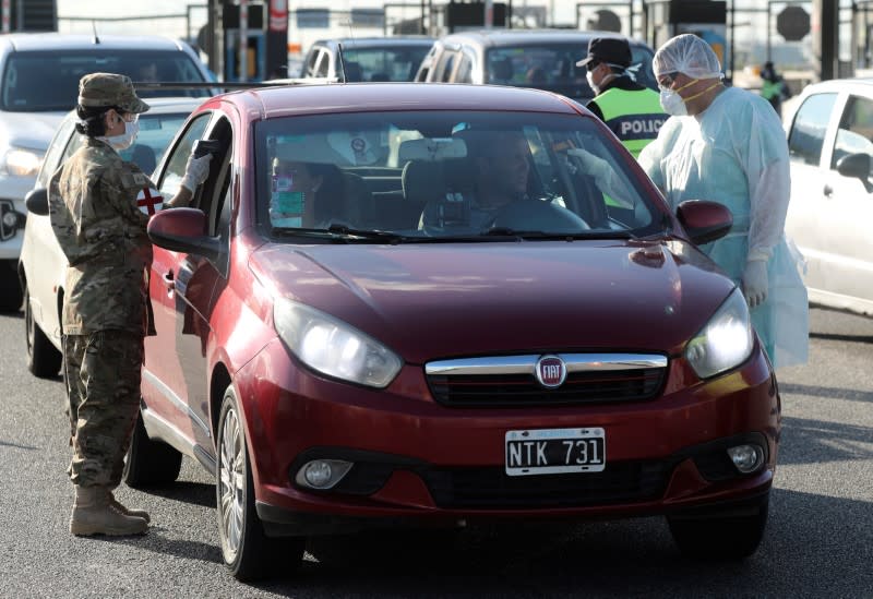 A member of the Argentine border police and a health worker take the temperature of a driver and his passenger, for precaution due to coronavirus disease (COVID-19), in Buenos Aires