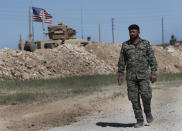 FILE - In this April 4, 2018 file photo, a U.S-backed Syrian Manbij Military Council soldier passes a U.S. position near the tense front line with Turkish-backed fighters, in Manbij, north Syria. Syria’s Kurds have been America’s partner in fighting the Islamic State group for nearly four years. Now they are furious over an abrupt U.S. troop pull-back that exposes them to a threatened attack by their nemesis, Turkey. The surprise U.S. pull-back from positions near the Turkish border, which began Monday, Oct. 7, 2019, stung even more because the Kurds have been abandoned before by the U.S. and other international allies on whose support they'd pinned their aspirations. (AP Photo/Hussein Malla, File)