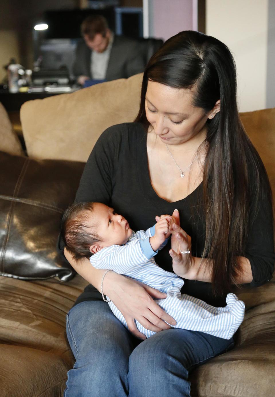 Jennifer Rogers, right, holds her baby Jack Nicolas Rogers as her husband, Nyle Rogers, left, works in his home office at their home in Edmond, Okla., Tuesday, Jan. 14, 2014. Jack Nicolas Rogers was born Dec. 21, 2013. Jennifer Rogers is formerly Jennifer Doan, a Plaza Towers schoolteacher who was the subject of what became an iconic photograph of the Moore, Okla. tornado as firefighters are shown freeing a debris-covered Doan from the rubble of a collapsed wall. Doan was pregnant with Jack Nicolas at the time. Jack's middle name, Nicolas, is in memory of one of her students, who died in the tornado. (AP Photo/Sue Ogrocki)