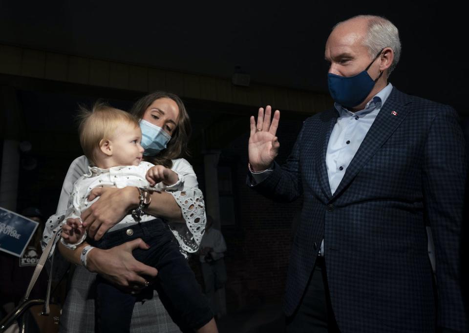 O'Toole, wearing a mask, waves to a baby held by his mother, also wearing a mask.