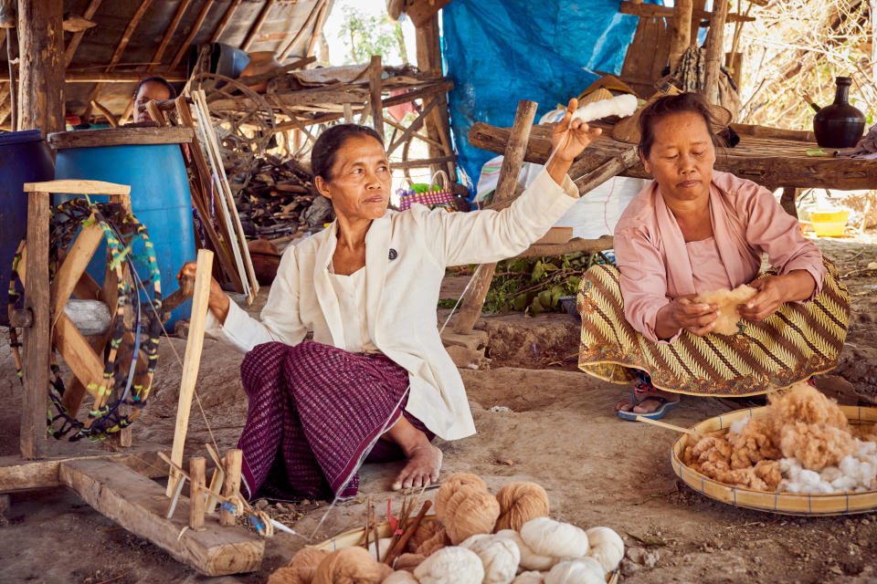 SukkhaCitta’s Ibu Kasmini, an Indonesian farmer who has inherited her farming practices from her grandmother, using a spinning wheel to turn cotton into threads while Ibu Karmini prepares the cotton behind her.