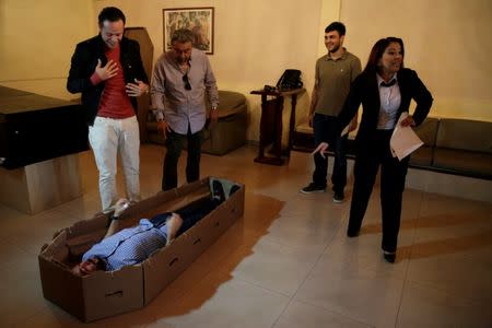 Elio Angulo (bottom L) lies inside a cardboard coffin next to Alejandro Blanchard (2nd L) as they introduce their product to potential customers at a mortuary in Valencia, in the state of Carabobo, Venezuela August 25, 2016. Picture taken August 25, 2016. REUTERS/Marco Bello