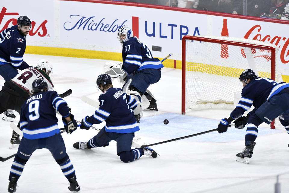 Arizona Coyotes' Nick Schmaltz (8) scores on Winnipeg Jets goaltender Connor Hellebuyck (37) as Jets' Vladislav Namestnikov (7) and Brenden Dillon (5) defend during the first period of an NHL hockey game in Winnipeg, Manitoba on Sunday, Feb. 25, 2024. (Fred Greenslade/The Canadian Press via AP)