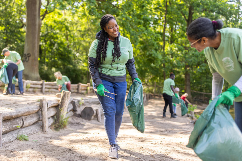 A group of people in casual clothing collect garbage in a park during a community cleanup