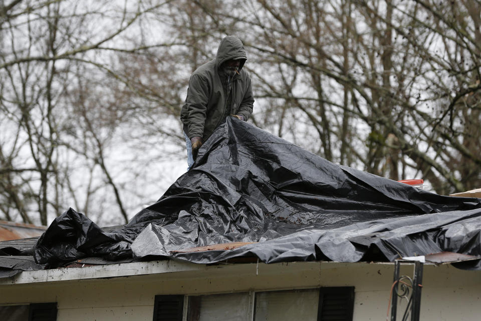 A roofer adjusts a protective tarp on a wind damaged roof in Pickens, Miss., Thursday, Feb. 6, 2020. Several homes and businesses in this North Central Mississippi city were hit with severe winds in a storm on Wednesday. (AP Photo/Rogelio V. Solis)