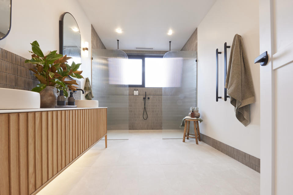 A shot of the bathroom with the wooden vanity on the left, the double shower on the far wall and a towel rack on the right.