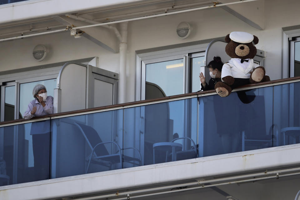 A woman with a teddy bear waves to another passenger quarantined on the Diamond Princess cruise ship in Yokohama, near Tokyo, Tuesday, Feb. 11, 2020. Japan's Health Minister Katsunobu Kato said the government was considering testing everyone remaining on board and crew on the Diamond Princess, which would require them to remain aboard until results were available. (AP Photo/Jae C. Hong)