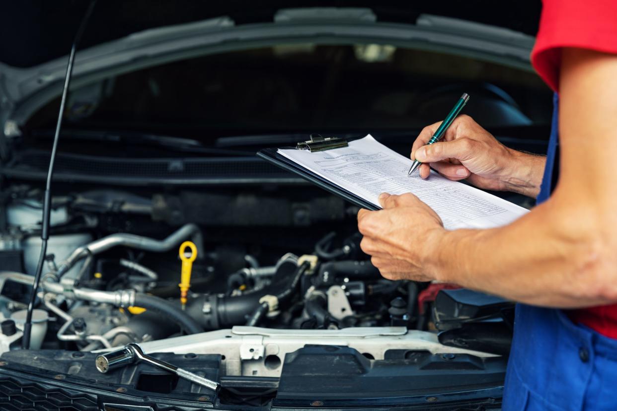 car maintenance and repair - mechanic writing checklist paper on clipboard