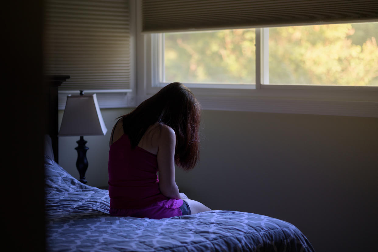 Petite woman with bowed head sitting on bed. Moody atmosphere, bad day, sadness and depression concept.