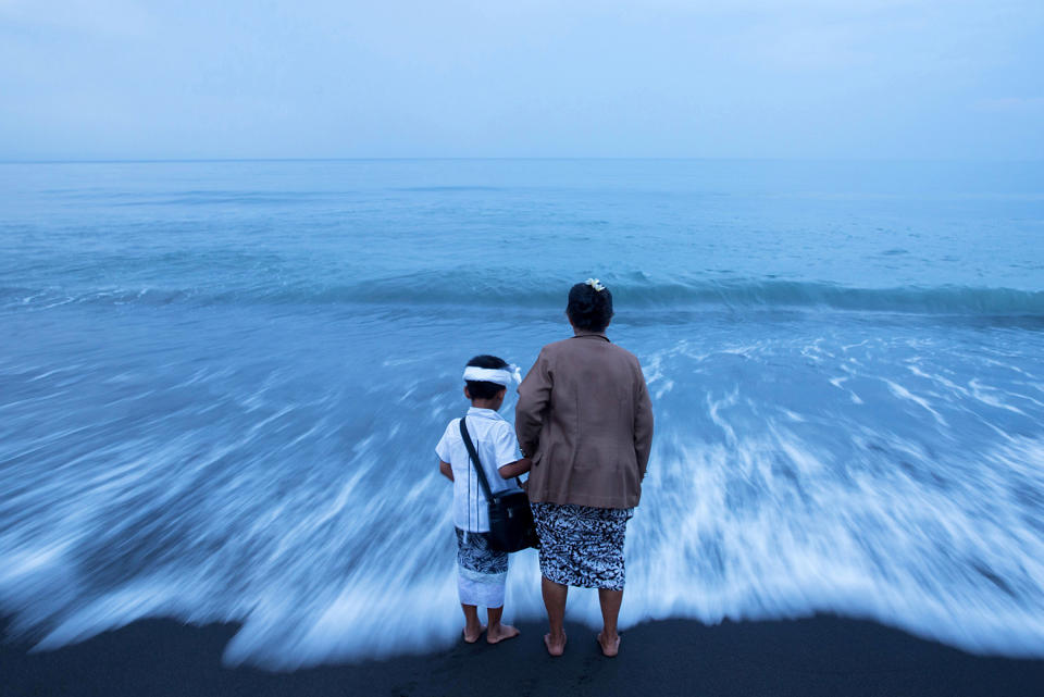 A Balinese Hindu woman hold her grandson’s hand on a beach in Bali