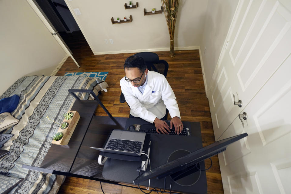 Medical director of Doctor on Demand Dr. Vibin Roy types notes as he listens to a patient during an online primary care visit from his home, Friday, April 23, 2021, in Keller, Texas. Some U.S. employers and insurers want you to make telemedicine your first choice for most doctor visits. Retail giant Amazon and several insurers have started or expanded virtual-first care plans to get people thinking telemedicine routinely, even for annual checkups. (AP Photo/LM Otero)