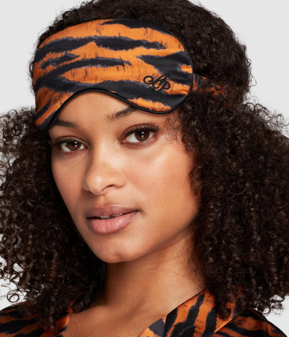 AP Tiger Sleep Mask from The Iconic. A woman with dark curly hair shows of the tiger-striped mask which matches her shirt.