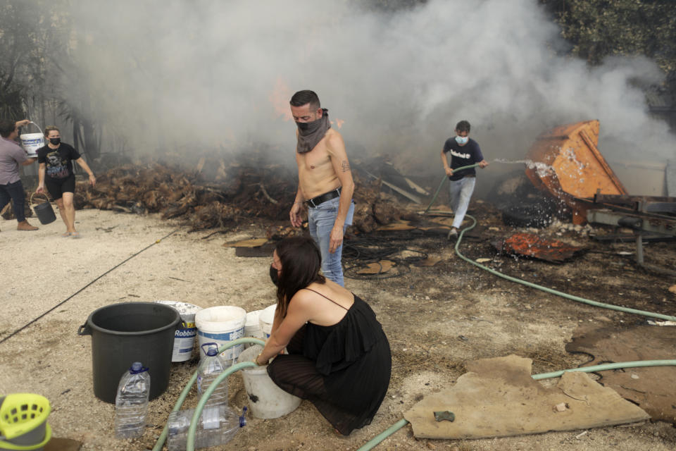 Local residents fill buckets with water to try to stop a forest fire from reaching their homes in the village of Figueiras, outside Leiria, central Portugal, Tuesday, July 12, 2022. Hundreds of firefighters in Portugal continue to battle fires in the center of the country that forced the evacuation of dozens of people from their homes mostly in villages around Santarem, Leiria and Pombal. (AP Photo/Joao Henriques)