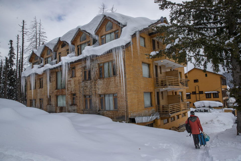 A Kashmiri tour operator carries luggage of a tourist as he walks toward a hotel at Gulmarg, northwest of Srinagar, Indian controlled Kashmir, Saturday, Jan. 9, 2021. Snow this winter has brought along with it thousands of locals and tourists to Indian-controlled Kashmir's high plateau, pastoral Gulmarg, which translates as “meadow of flowers." (AP Photo/ Dar Yasin)