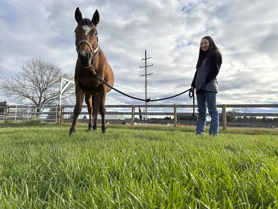 Kylie Ossege smiles while standing next to her horse, Blaze, at a boarding facility Saturday, Nov. 11, 2023, in Mayfield Township, Mich. Ossege was severely injured in a 2021 mass shooting at Oxford High School and says spending time with Blaze provides her with a measure of comfort. (AP Photo/Mike Householder)