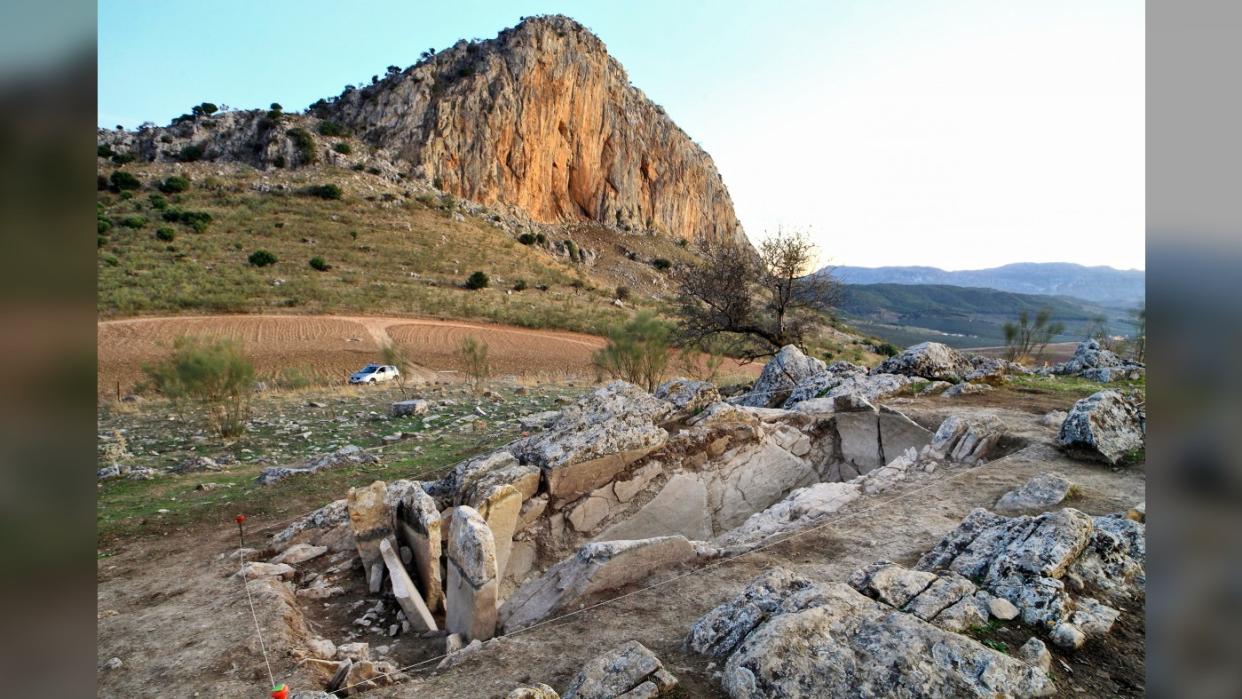  Archaeologists found the 5,400 year-old stone tomb in the "neck" area of a prominent mountain that looks from some angles like the head of a sleeping giant. In the foreground we see the opening on a tomb. In the background we see the prominent mountain known as La Peña de los Enamorados (the Rock of the Lovers) found in Spain. 