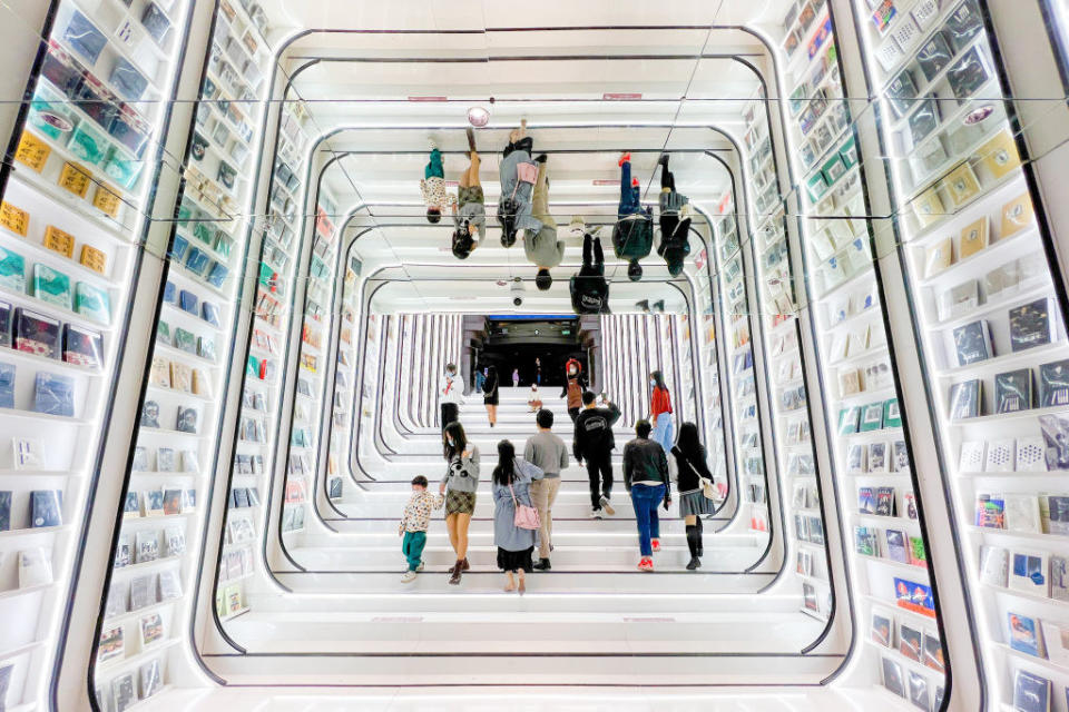 tunnel of bookshelves that are lit up along the side with a mirrored ceiling