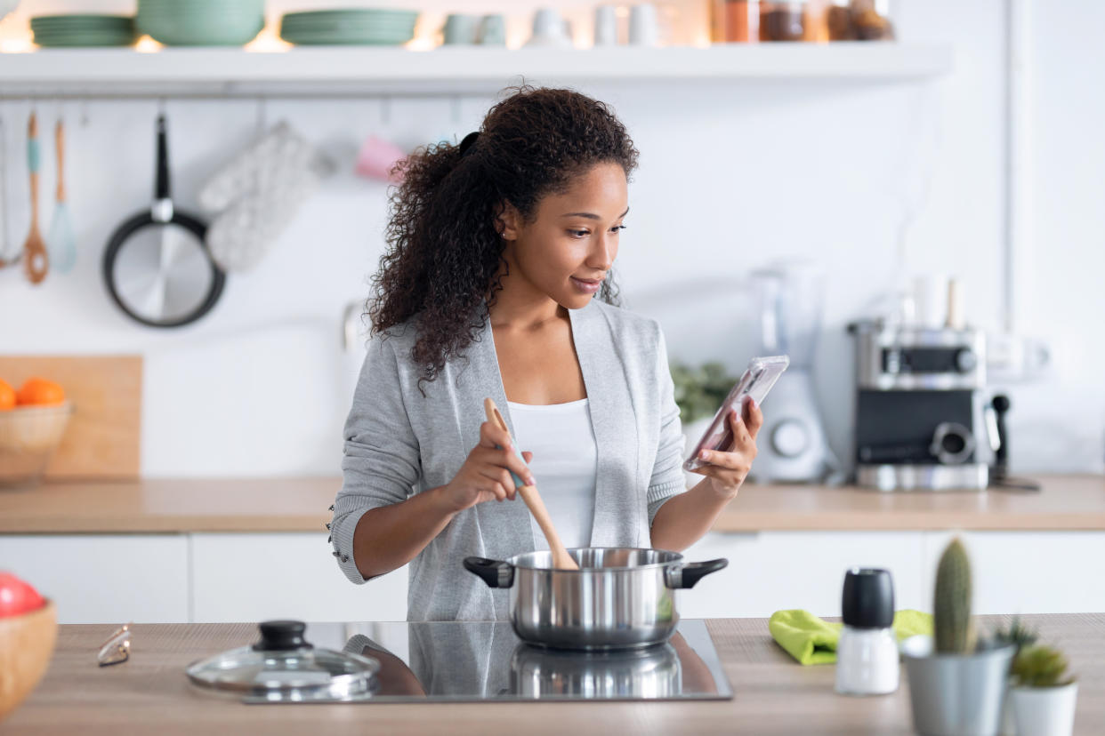 Shot of confident young african american woman cooking healthy food while using her mobile phone in the kitchen at home.