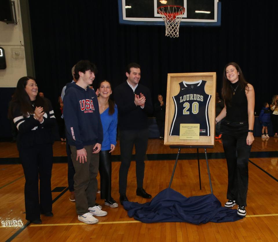 Joined by her family, Maddy Siegrist poses beside her No. 20 jersey that was retired during a ceremony at Our Lady of Lourdes High School on January 4, 2024.