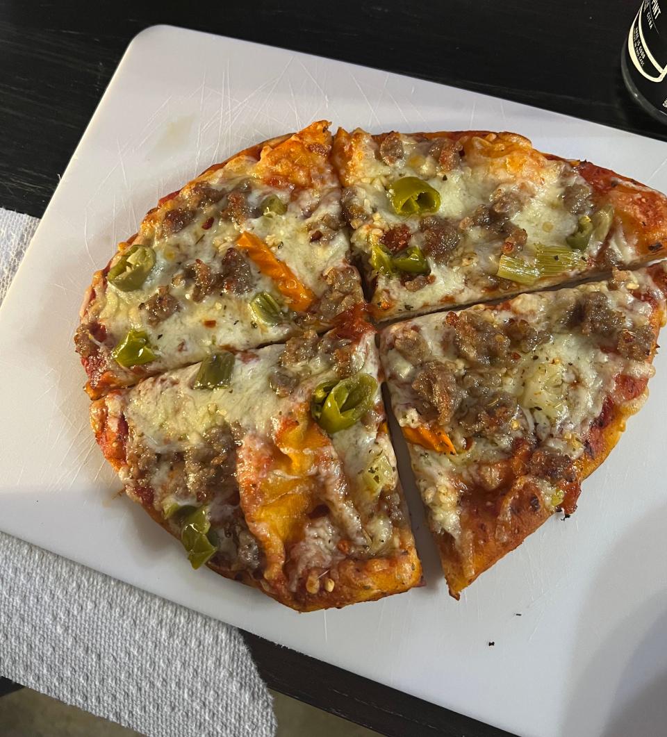 A partially eaten pizza with pepperoni, sausage, and green peppers on a white cutting board next to a small yellow toy truck