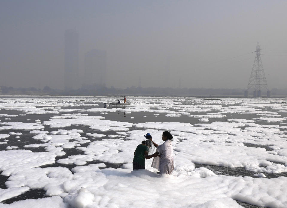 FILE - A woman bathes her daughter in the Yamuna River, covered by a chemical foam caused by industrial and domestic pollution as the skyline is enveloped in toxic smog, in New Delhi, India, on Nov. 17, 2021. . A new study says Earth has pushed past seven out of eight scientifically established safety limits and into “the danger zone,” not just for an overheating planet that’s losing its natural areas, but for well-being of people living on it. The study, published Wednesday, May 31, 2023, for the first time it includes measures of “justice,” which is mostly about preventing harm for groups of people. (AP Photo/Manish Swarup)