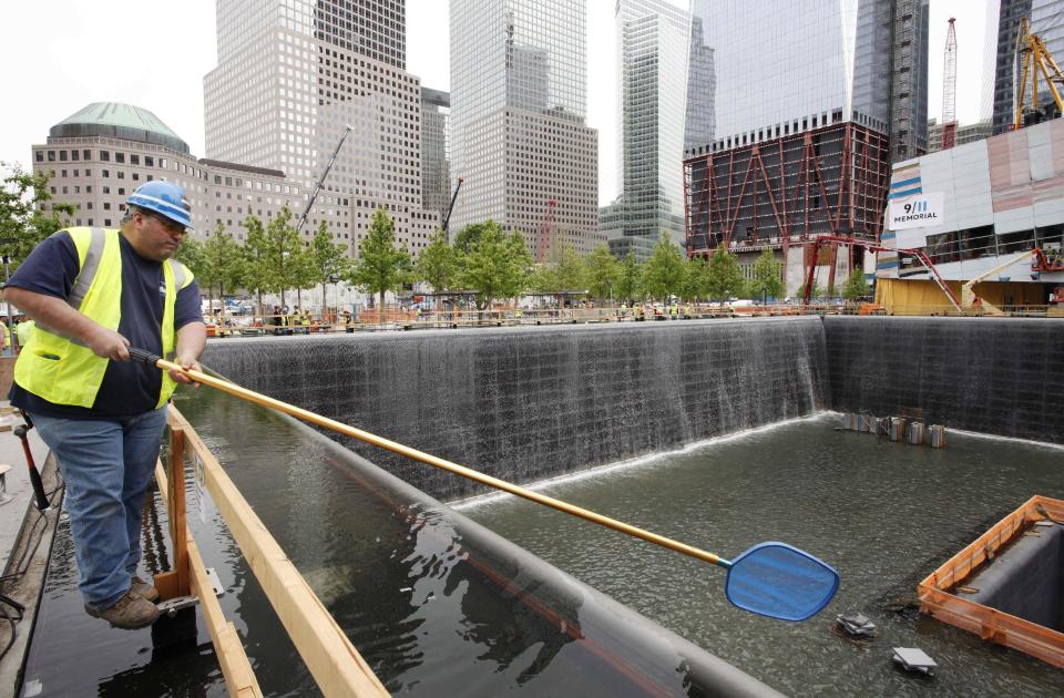 FILE - In this May 13, 2011 file photo, Anthony St. Jeanos, left, uses a net to skim debris from the water during a test of the waterfalls at the National September 11 Memorial, at the World Trade Center site in New York. The foundation that runs the memorial estimates that once the roughly $700 million project is complete, it will cost $60 million a year to operate. (AP Photo/Mark Lennihan, File)