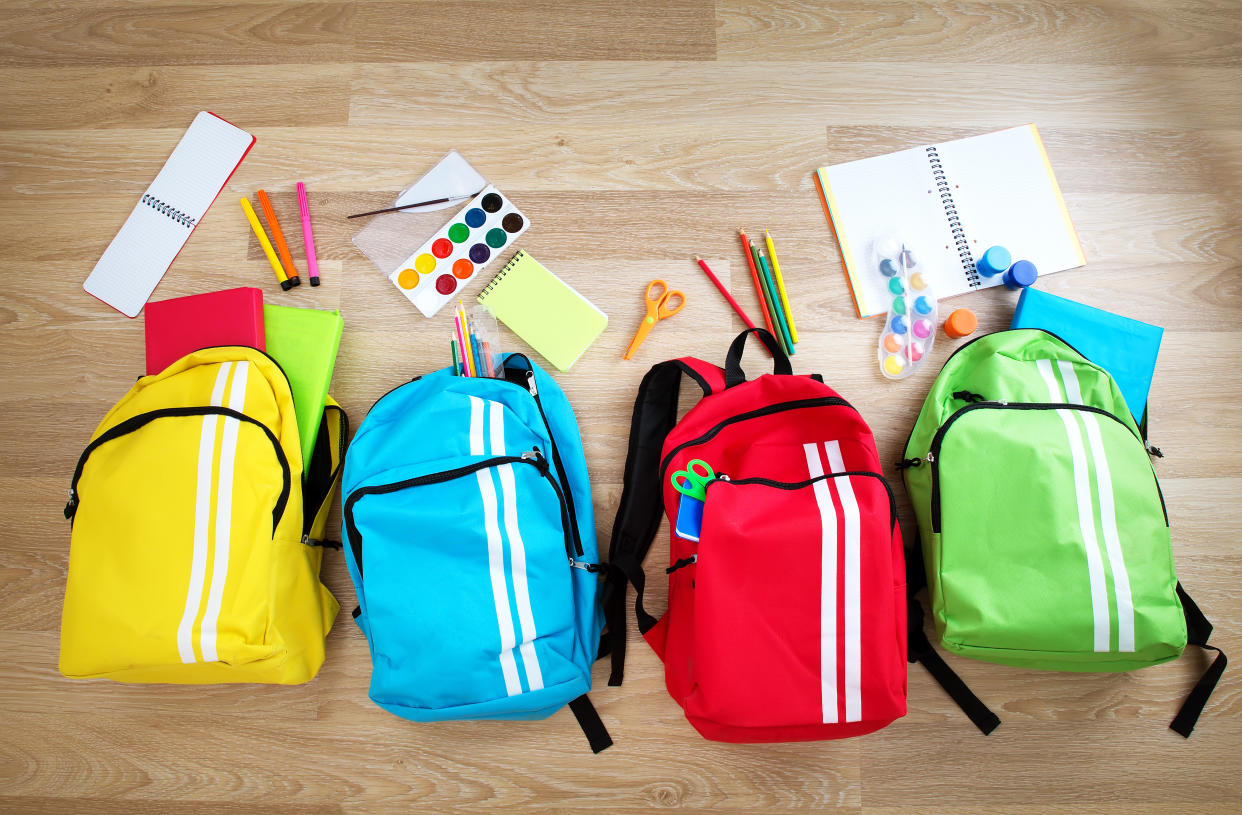 Colourful children schoolbags on wooden floor. Backpacks with school accessories