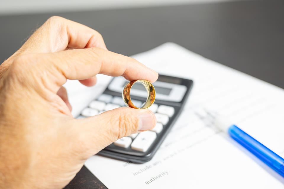 Hand holds a gold ring over a calculator and a document, next to a pen