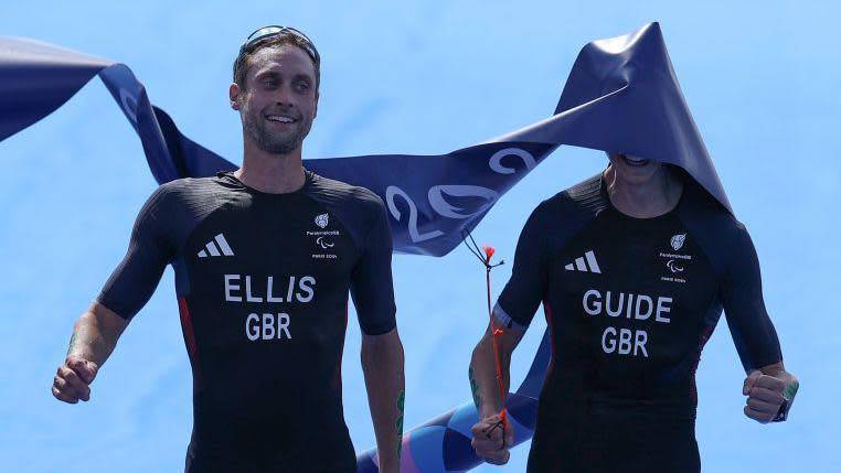 Dave Ellis and Luke Pollard cross the Paralympic triathlon finish line, with Pollard's face obscured by the tape they have just crossed at the finish