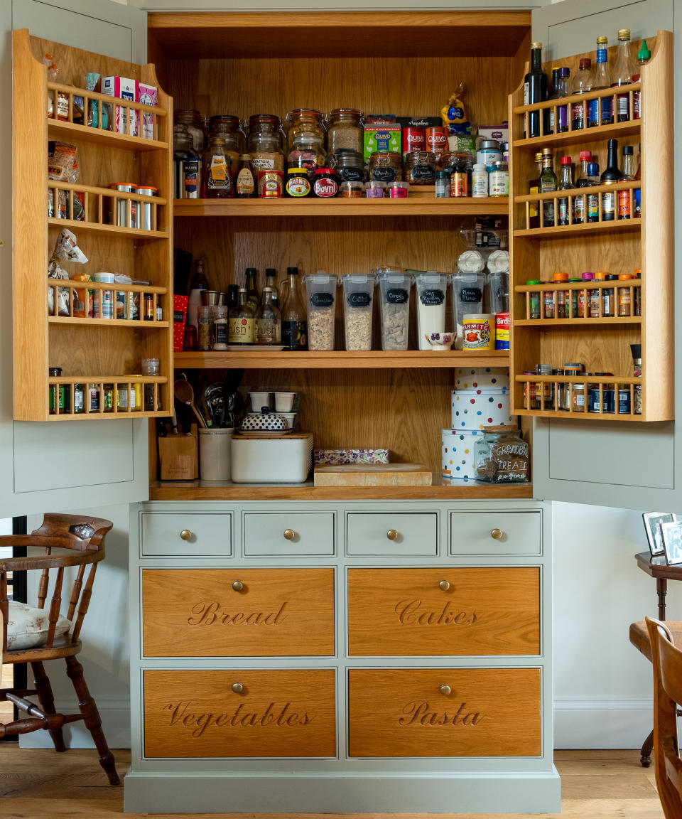 Pantry with open doors with shelving on doors and shelves with food and storage and labeled containers and drawer below