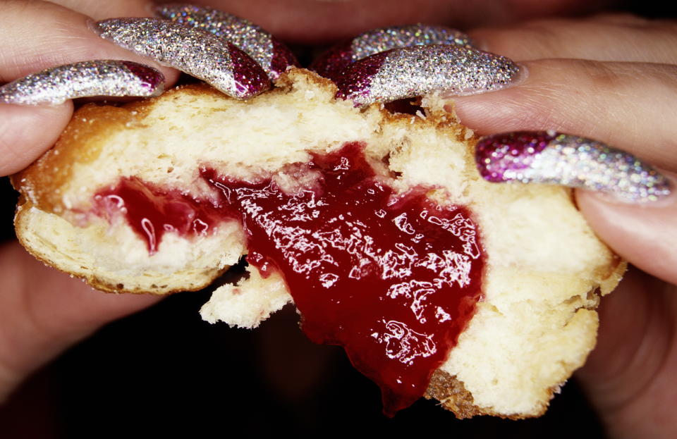 Woman with long glittery nails eating jam doughnut, close-up