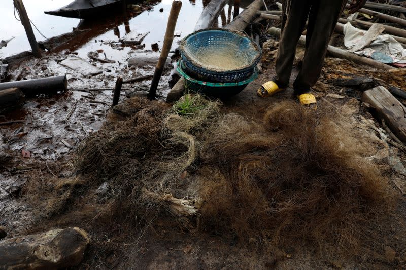 Benson Daniel, Community Development Chairman, Sandsand fishing settlement, stands behind oil-soaked fishing net at Sandsand, in Nembe, Bayelsa