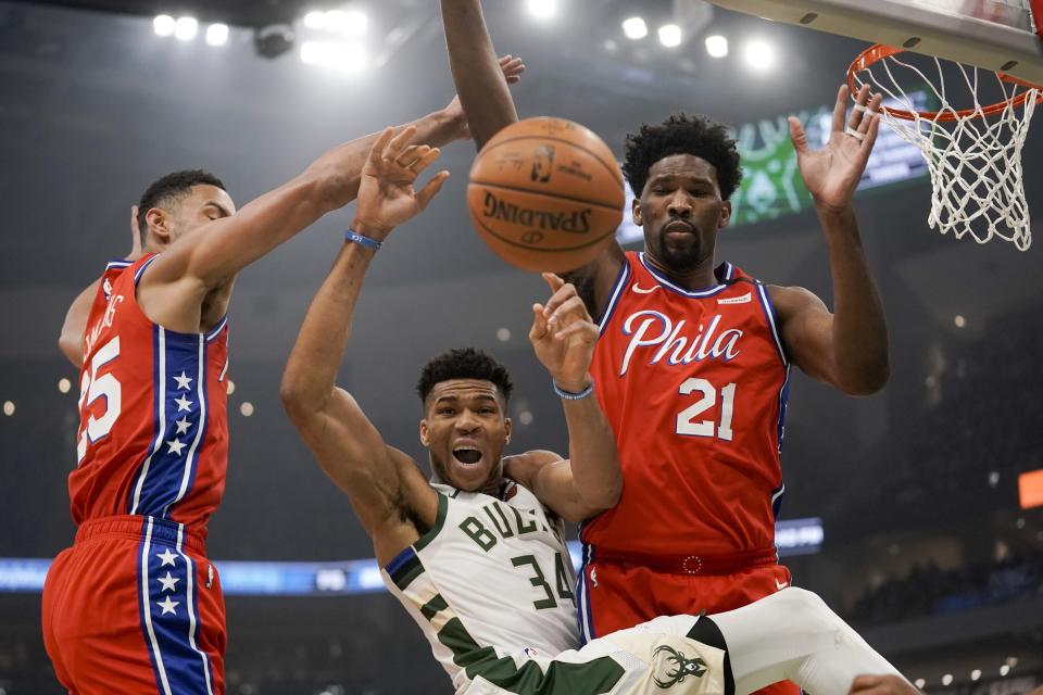 Milwaukee Bucks' Giannis Antetokounmpo is fouled as he drives between Philadelphia 76ers' Ben Simmons and Joel Embiid (21) during the first half of an NBA basketball game Saturday, Feb. 22, 2020, in Milwaukee. (AP Photo/Morry Gash)