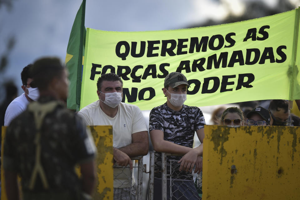 Demonstrators stand with a banner that reads in Portuguese "We want the Army in power" at the Alvorada palace, after a protest demanding for military intervention during the new coronavirus emergency, in Brasilia, Brazil, Sunday, April 19, 2020. Bolsonaro came out in support of a small protest Sunday that defended military intervention, infringing his own ministry's recommendations to maintain social distancing and prompting fierce critics. (AP Photo/Andre Borges)