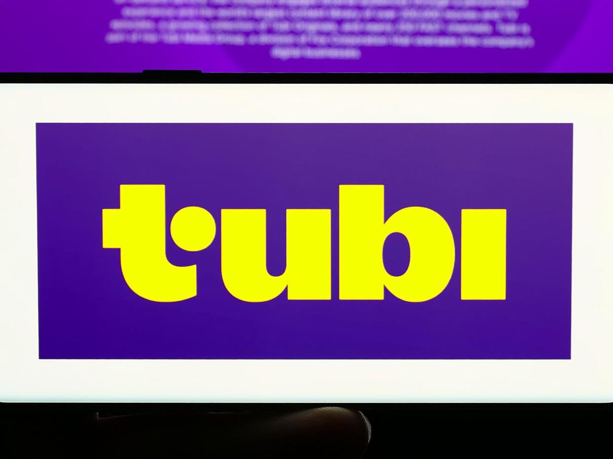 Person holding cellphone with logo of US streaming platform company Tubi Inc. in front of business webpage. Focus on phone display.