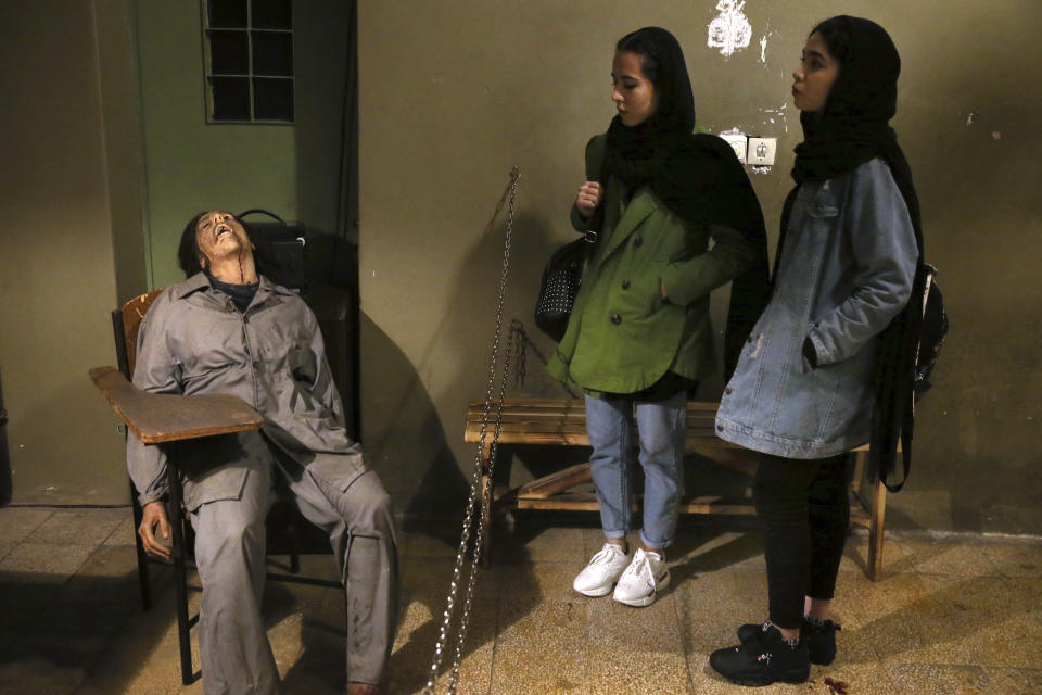 In this Monday, Jan. 7, 2019 photo, women look at an exhibition at a former prison run by the pre-revolution intelligence service, SAVAK, now a museum, where a wax mannequin of a tortured female prisoner is on display, in downtown Tehran, Iran. As Iran marks the 40th anniversary of its Islamic Revolution and the overthrow of the shah, those who suffered torture at the hands of the police and dreaded SAVAK still bear the scars. U.N. investigators and rights group say that even today, Iran tortures and arbitrarily detains prisoners. (AP Photo/Ebrahim Noroozi)