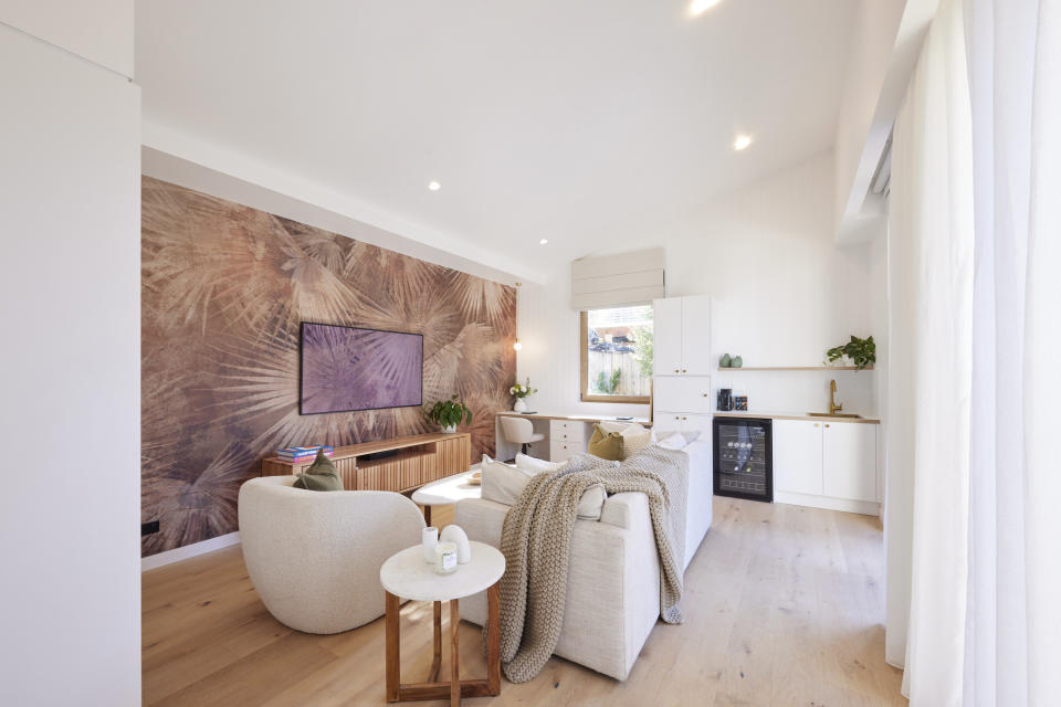 A wide shot of the studio with a floral wallpaper a couch in the middle and small kitchen on the far wall. 