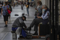A shoe shiner brushes a client's shoes in downtown Madrid, Spain, Wednesday, Sept. 30, 2020. The Spanish capital and its suburbs, the region in Europe where a second coronavirus wave is expanding by far the fastest, are edging closer to stricter mobility curbs and limits on social gatherings after days of a political row that has angered many Spaniards. (AP Photo/Bernat Armangue)