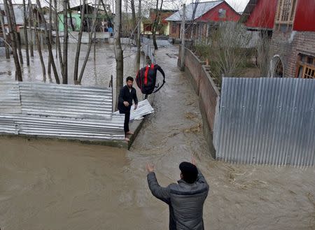 A man throws his belongings towards another to be moved to a safer place at a flooded neighbourhood after incessant rains in Srinagar March 30, 2015. REUTERS/Danish Ismail