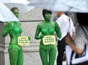 Shoppers look on as two animal rights activists in green body painting protest outside a luxury brand store in Taipei on October 20, 2011. The activists urged luxury houses to stop selling products made from exotic animal skins to protect the animals from cruelty during the manufacturing process. AFP PHOTO / PATRICK LIN