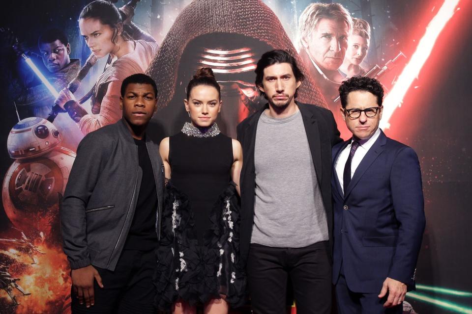 john boyega, daisy ridley, adam driver, and jj abrams pose for a photo while standing in front of a star wars movie background