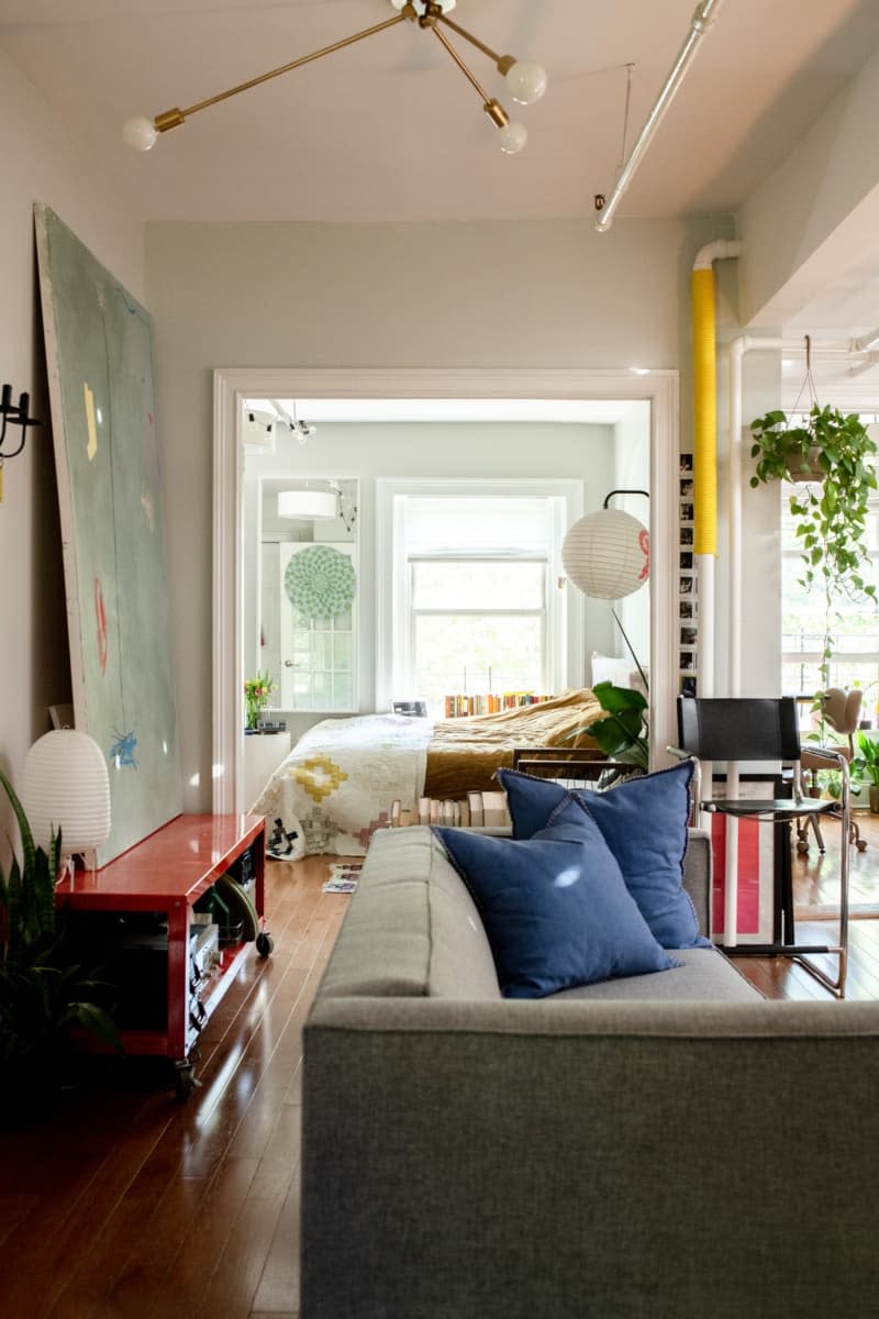 Living room with a grey couch and blue pillows near a large wall-sized piece of art on a red cart.