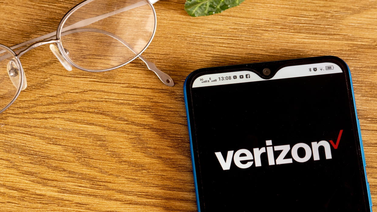  Verizon logo shown on smartphone next to a pair of glasses 