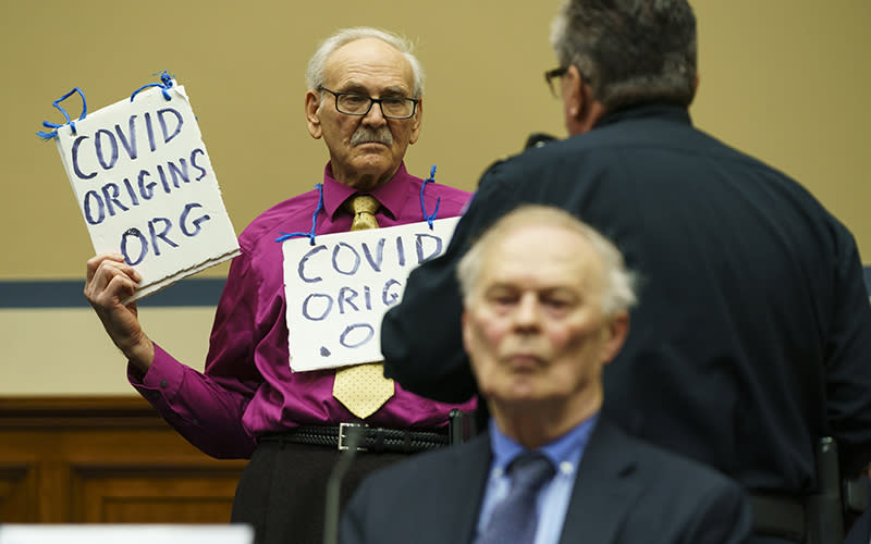 A protester holds up a sign during a committee meeting to discuss the origins of the coronavirus