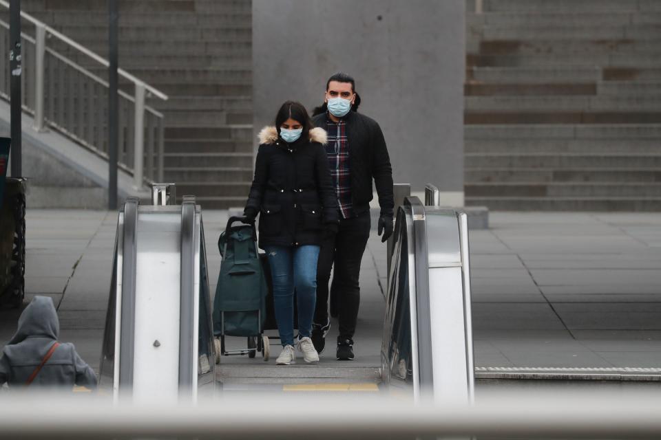 A couple wearing a protective facemask walks at La Defense, near Paris, on March 16, 2020, while protective measures are taken in France against the spread of the COVID-19. - France has closed down all schools, theatres, cinemas and shops not selling "non-essential" items such as food in an effort to stop the spread of the virus. (Photo by Ludovic Marin / AFP) (Photo by LUDOVIC MARIN/AFP via Getty Images)