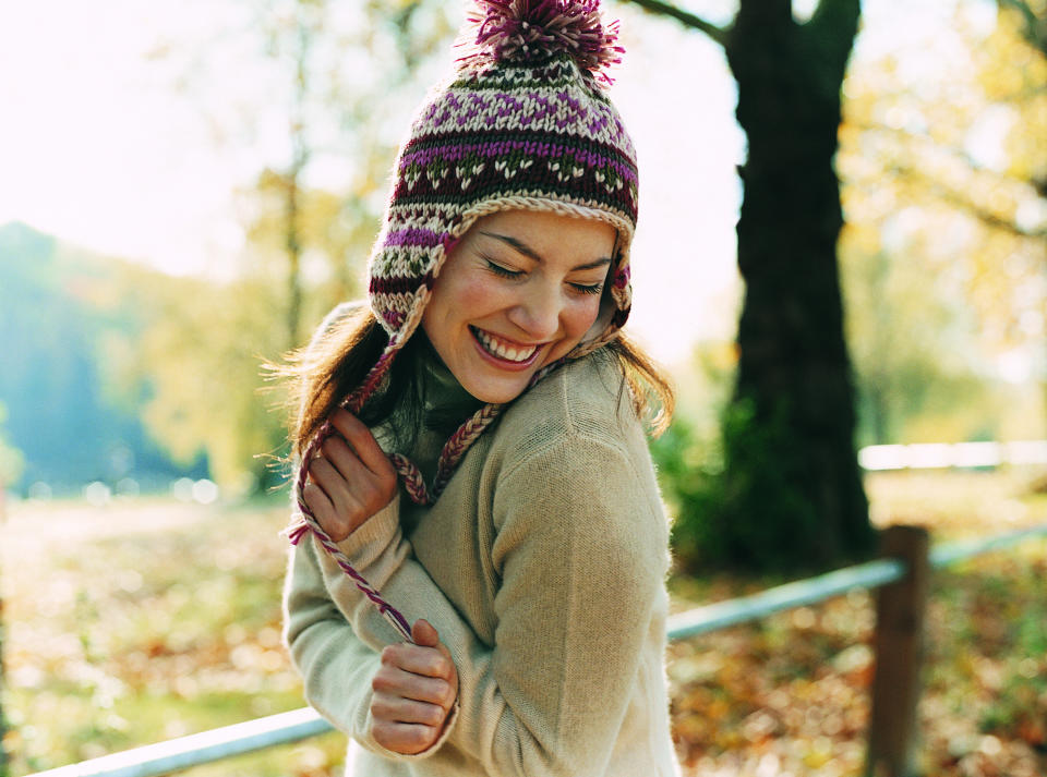 Young woman in bobble hat and sweater smiling in a fall landscape.