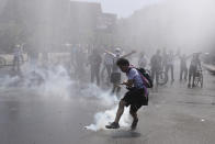 A protester kicks a tear gas canister during clashes with police in Santiago, Chile, Sunday, Oct. 20, 2019. Protests in the country have spilled over into a new day, even after President Sebastian Pinera cancelled the subway fare hike that prompted massive and violent demonstrations. (AP Photo/Esteban Felix)