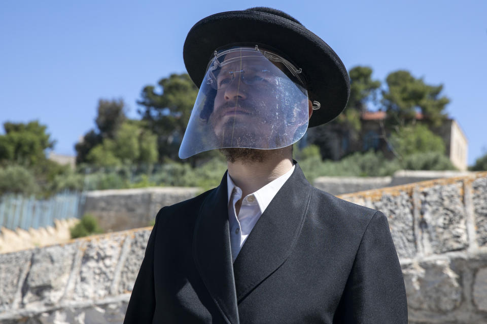 In this Friday, May 1, 2020 photo, a relative of a man who died from the coronavirus in the USA wears a face shield after the burial in east Jerusalem's Mount of Olives cemetery. Air travel to Israel has come to a near standstill due to coronavirus restrictions, but one type of voyage still endures: the final journey of Jews wishing to be buried in Israel. Families, the aviation industry and health workers are finding ways to keep the deceased flying in despite the challenges presented by the virus. (AP Photo/Ariel Schalit)