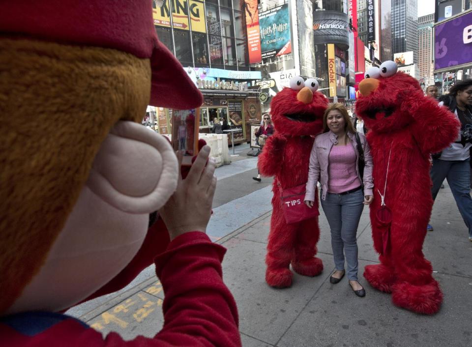 A Super Mario character, left, uses a woman's mobile phone camera to photographer her with a pair of Elmo characters in New York's Times Square,  Tuesday, April 9, 2013. A string of arrests in the last few months has brought unwelcome attention to the growing number of people, mostly poor immigrants, who make a living by donning character outfits, roaming Times Square and charging tourists a few dollars to pose with them in photos. (AP Photo/Richard Drew)